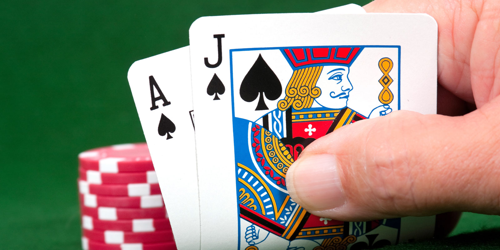 A hand holding a pair of cards with poker chips on the green felt.