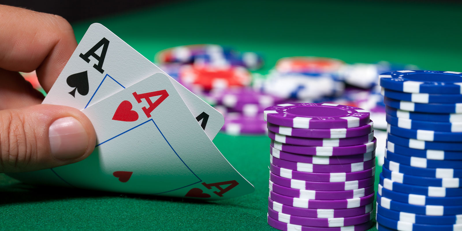 Hand holding poker cards on a green felt table.