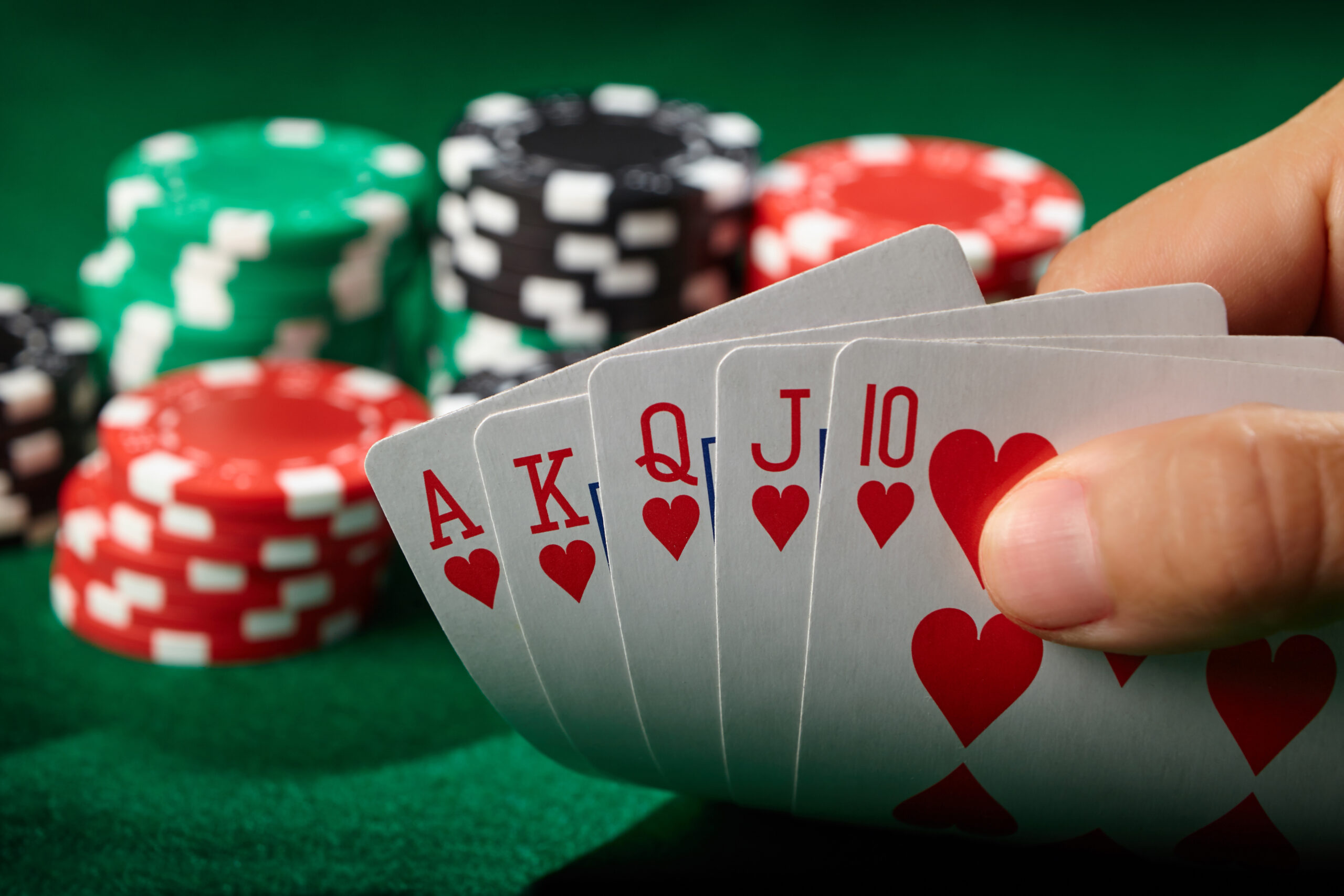 A hand holding a royal flush with poker chips behind.