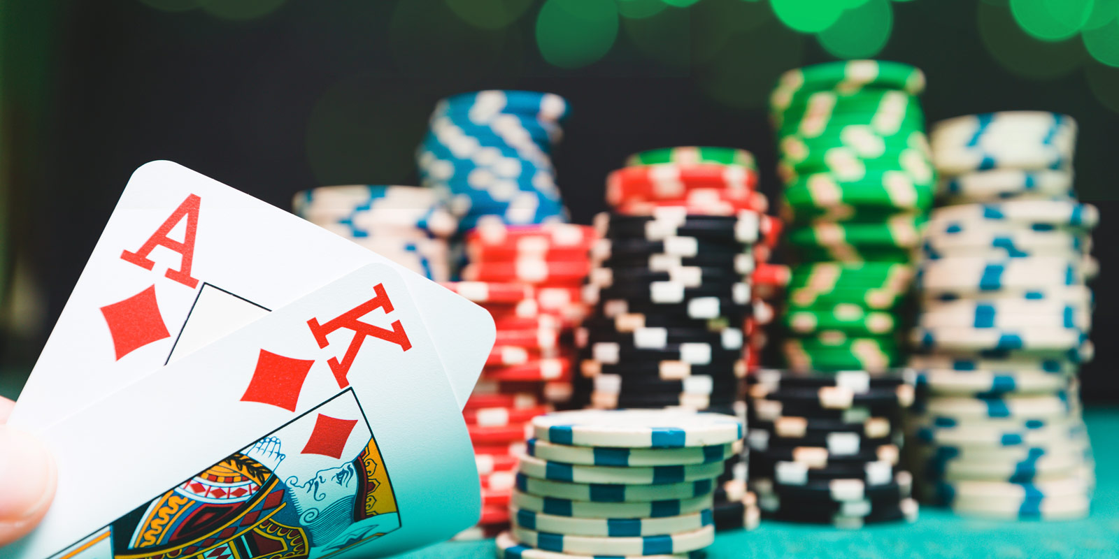A hand holding an Ace and a King playing card with poker chips in the background on a green felt table.